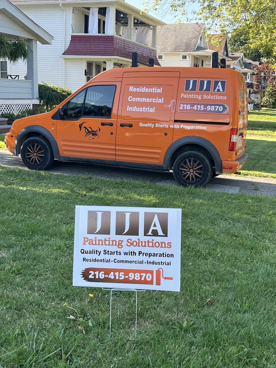 The orange JJA Painting Solutions work van parked on a street, with a white JJA lawn sign on the grass in front.